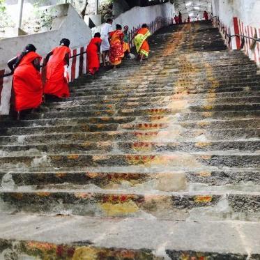 People in bright orange walk up a long staircase of old stone steps to a temple.